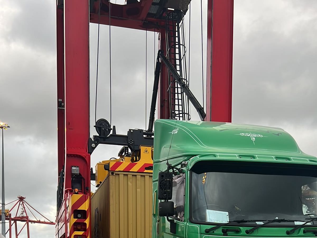 An Aardiv truck collecting a container beneath the straddle carriers at a container terminal