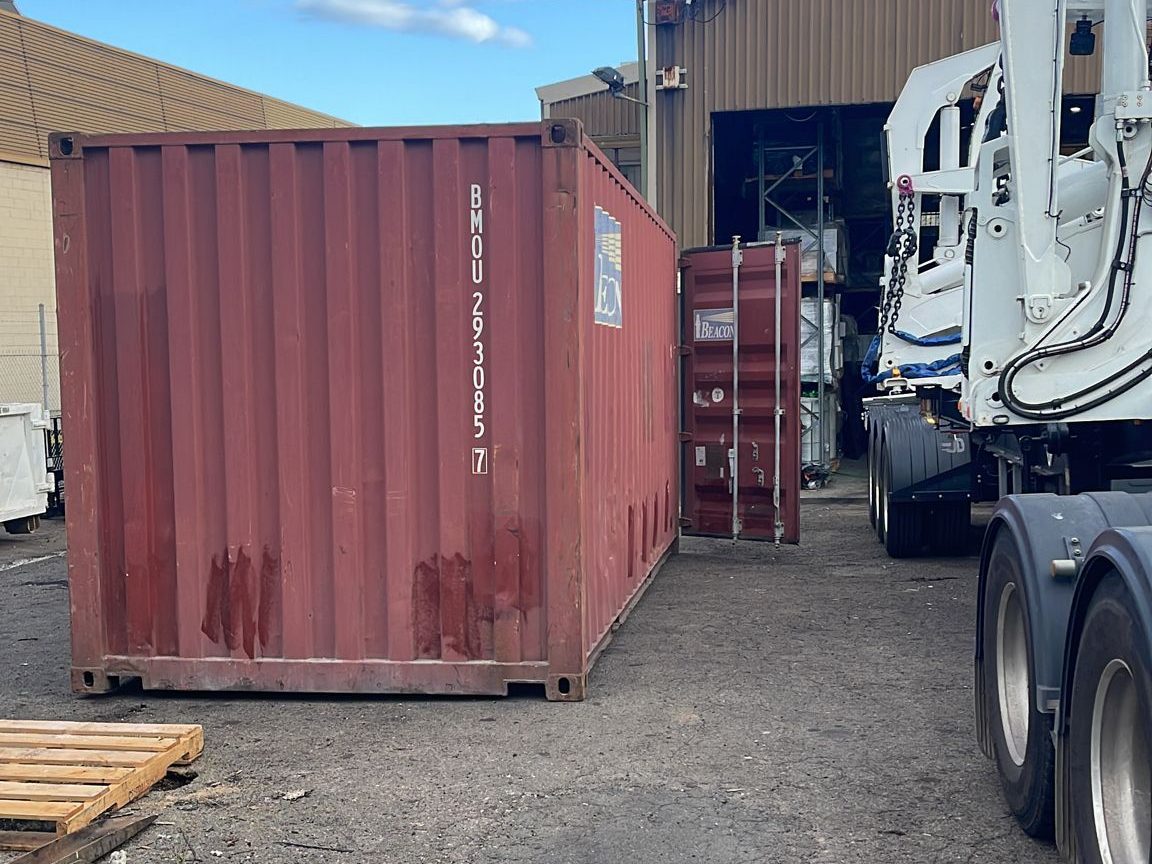 A 20-foot container standing on the ground beside a side loader trailer