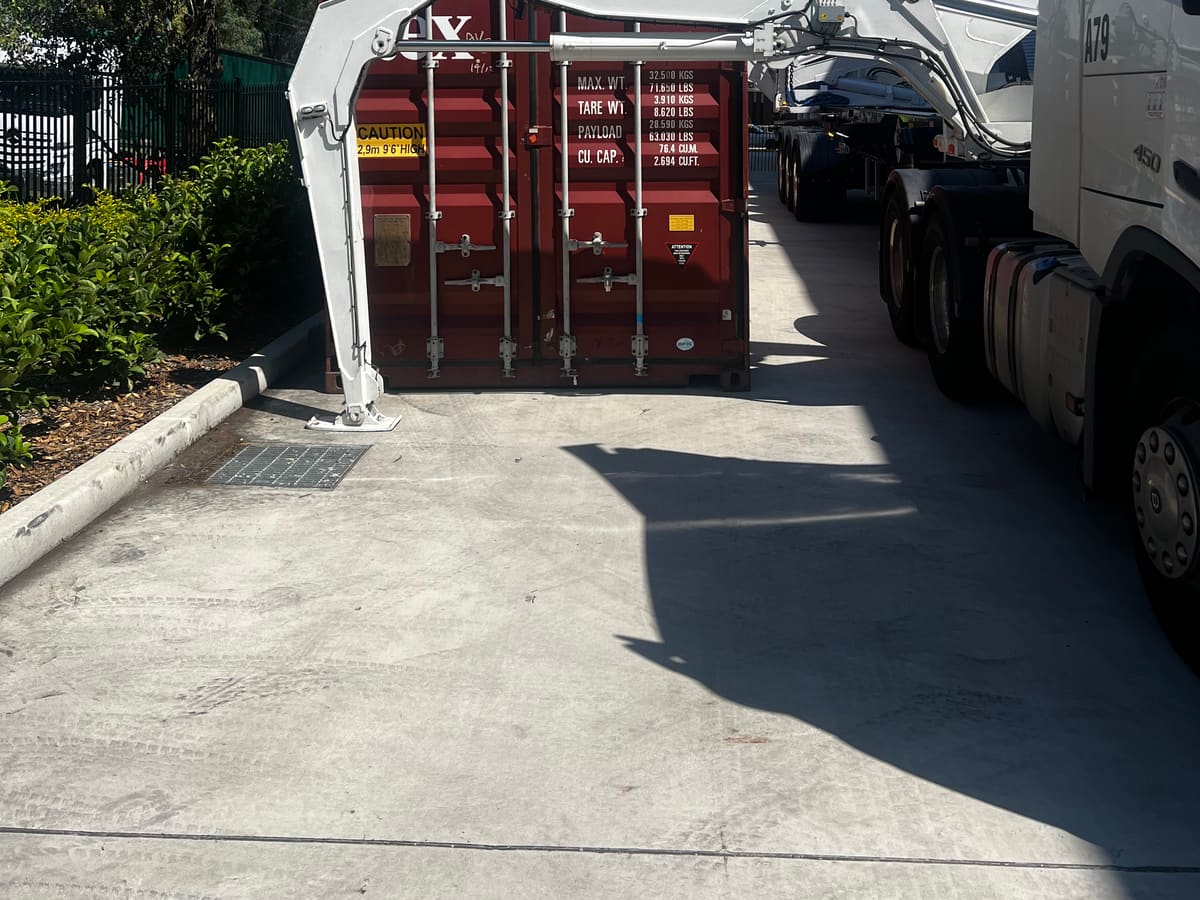 A side loader placing a shipping container on the ground in a narrow driveway